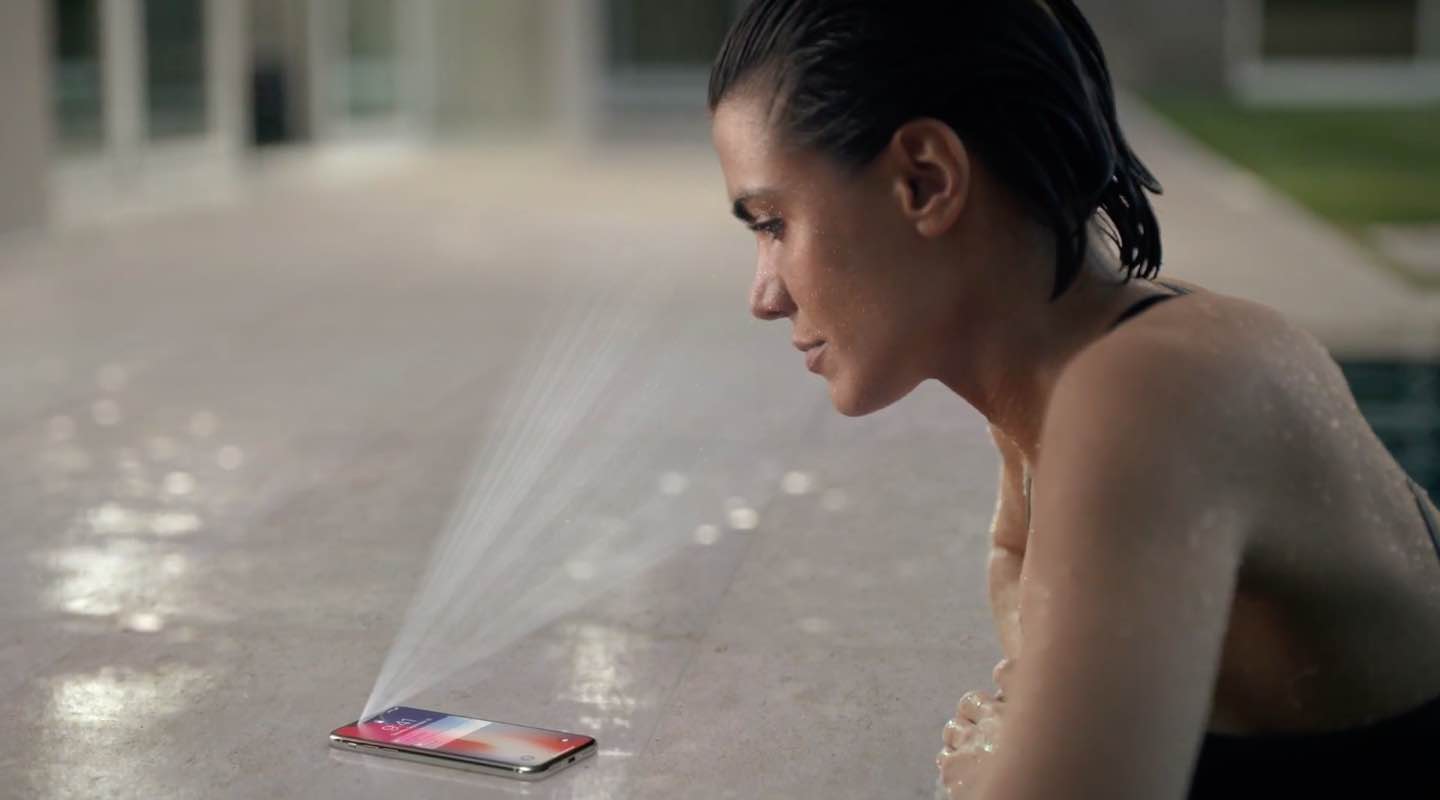 A still from Apples iPhone X ad showing a woman by the poolside using Face ID to unlock her phone