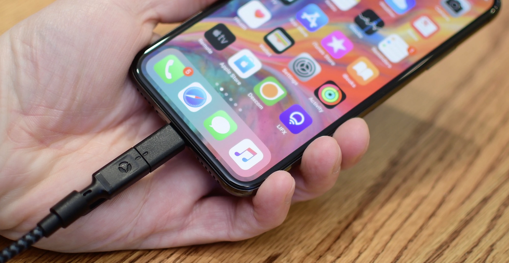 A close up of an iPhone X with a cable being plugged into the Lightning port