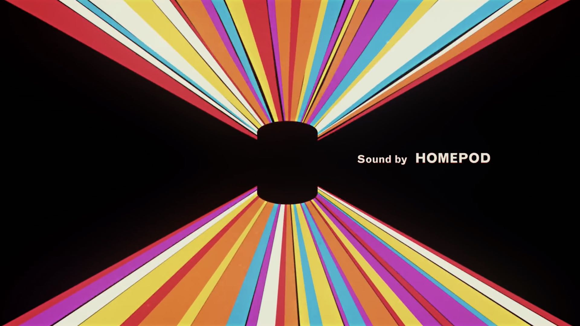 An image taken from Apple's introductory video for HomePod, showing the smart speaker set against a black background with colorful light streaks and the tagline "Sound by HomePod"