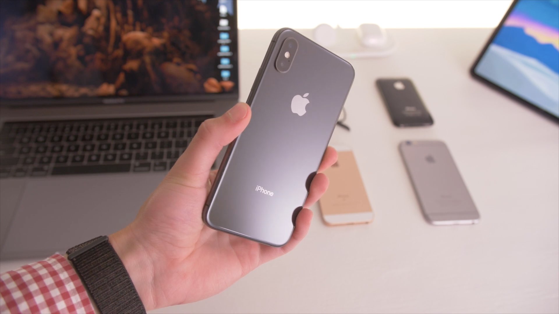 iPhone XS held in a young person's hand with a work desk seen blurred in the background