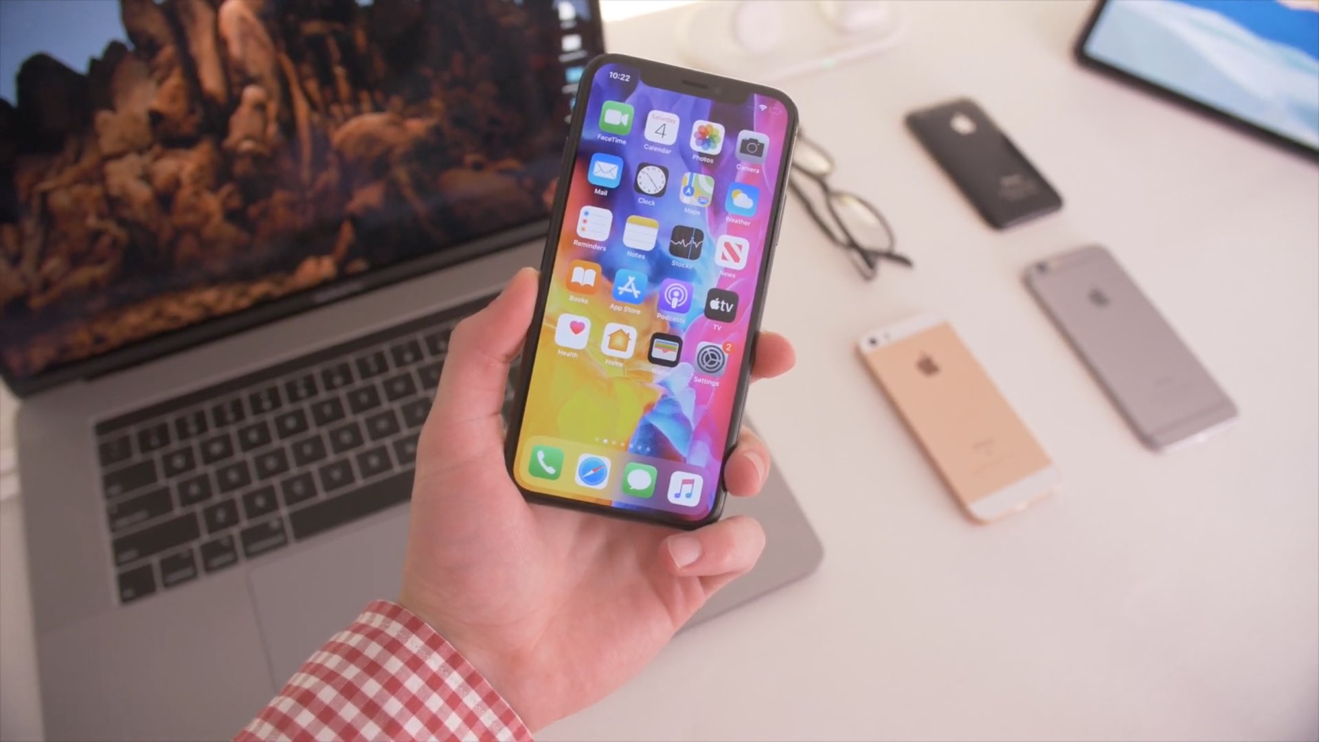 An iPhone XS held in hand with the Home Screen shown on the display