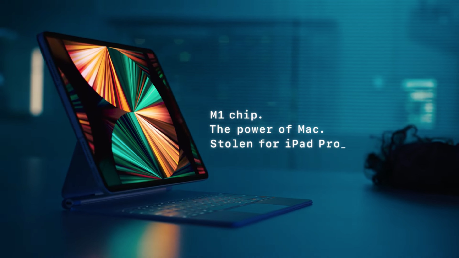 A still image grabbed from the closing scene of Apple's video advertisement featuring an iPad Pro with a Magic Keyboard sitting on a desk, with the tagline "M1 chip. The power of Mac. Stolen for iPad Pro" displayed in white font
