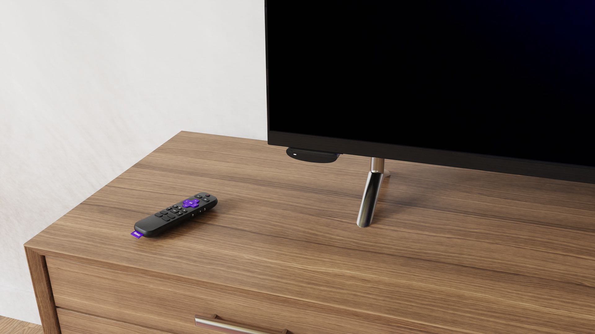 A lifestyle photograph showing Roku's Voice Remote Pro laying flat on a TV cabinet next to a TV set with a Roku Express 4K+ streaming player connected to it