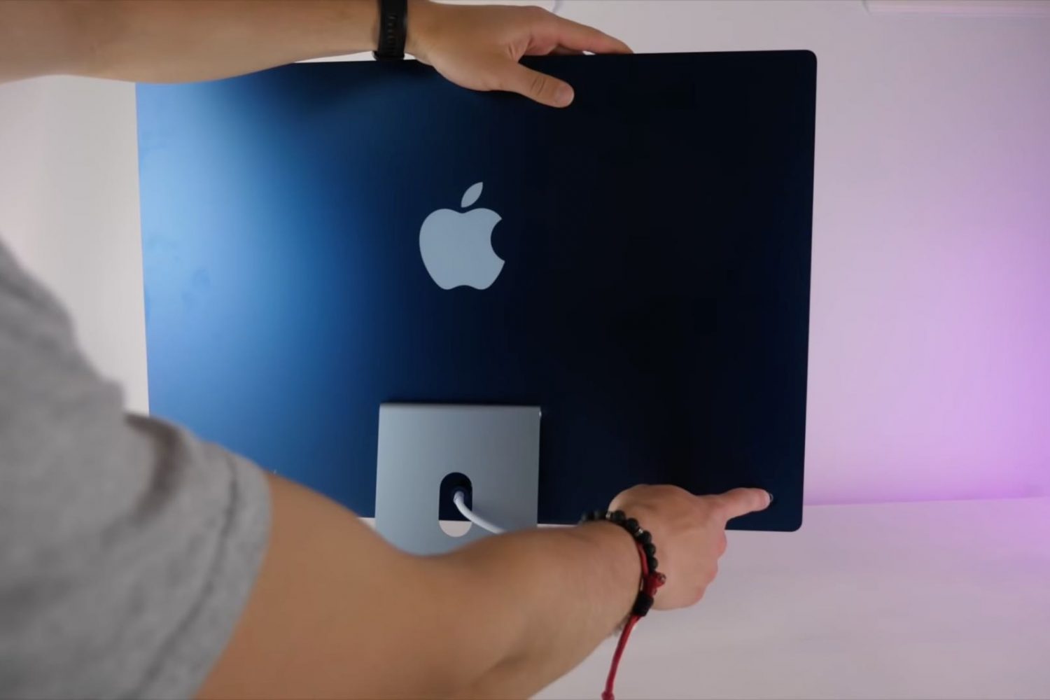 A photograph showing the backside of a blue 24-inch Apple M1 iMac computer with a finger touching the power button