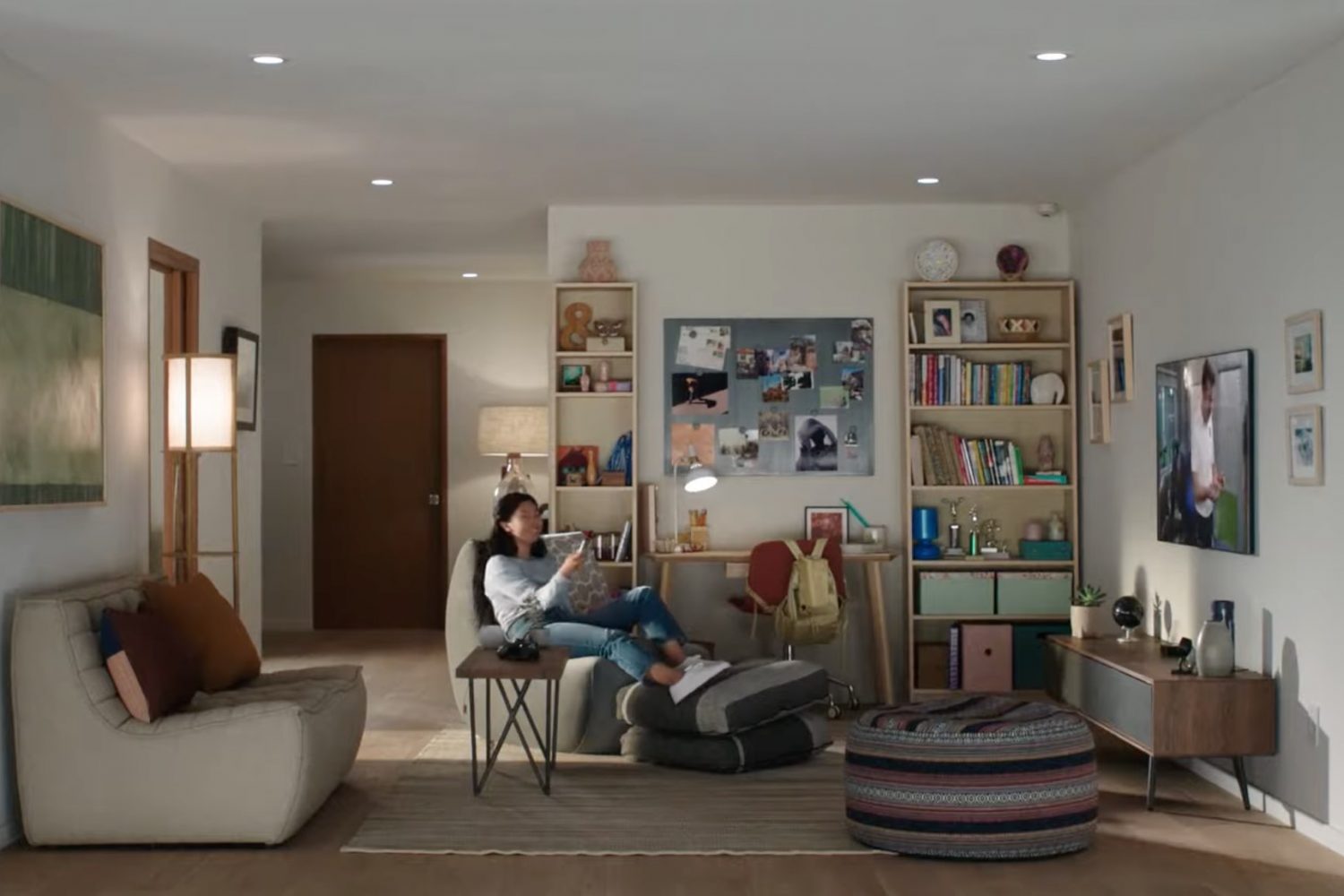 A lifestyle image showing a home featuring a young woman sitting on the couch, smiling and watching Apple TV and holding Siri Remote in her right hand