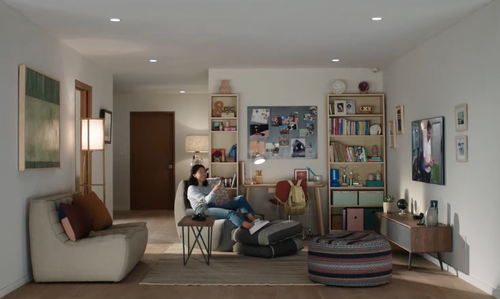A lifestyle image showing a home featuring a young woman sitting on the couch, smiling and watching Apple TV and holding Siri Remote in her right hand