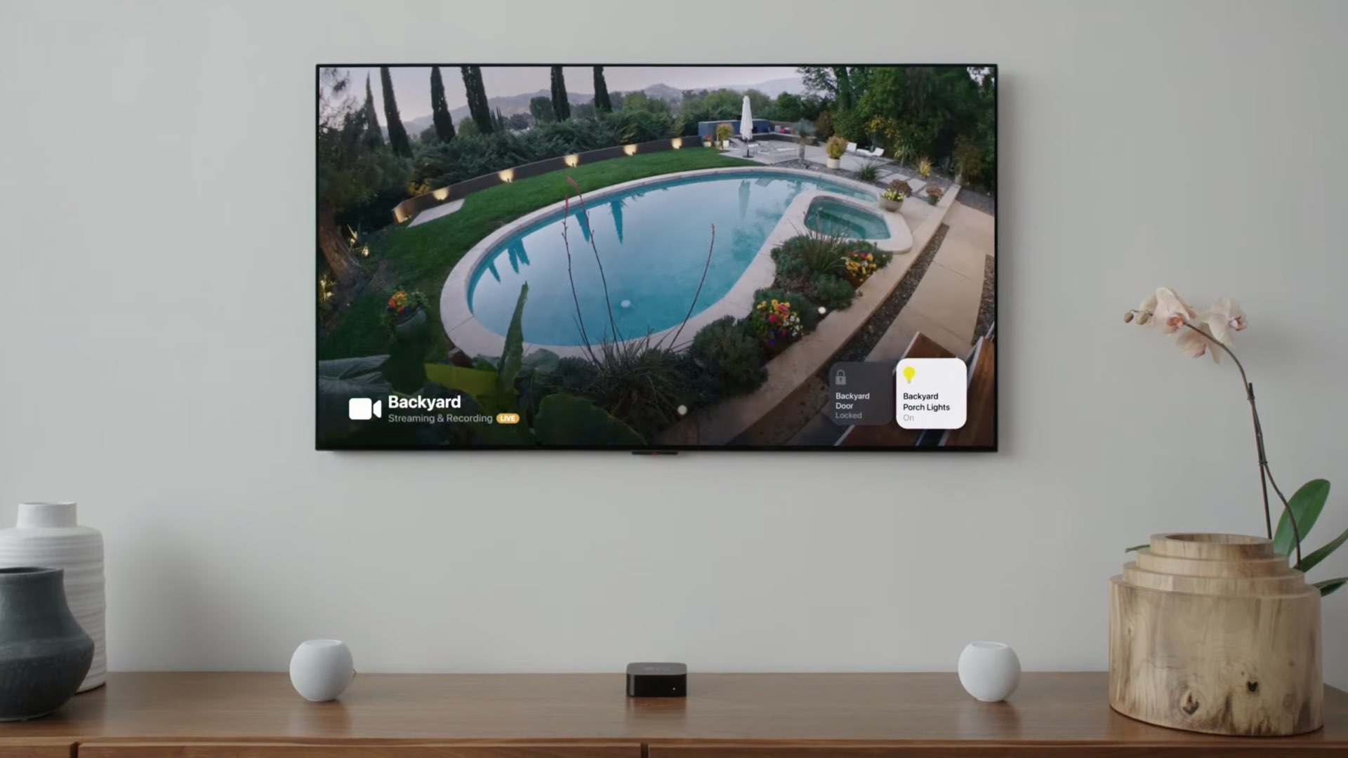 An image showing a HomeKit security camera feed displayed on Apple TV with tvOS 15, with smart lighting controls visible in screen corners