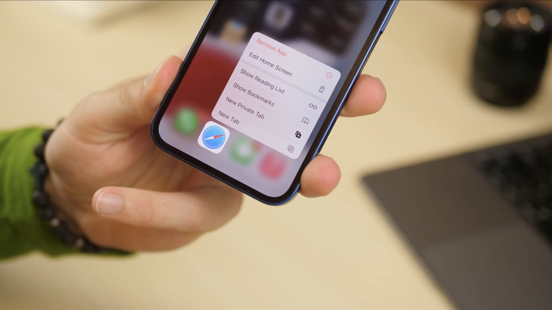 A photo displaying an iPhone held in hand with the contextual menu for iOS 15 Safari shown on iPhone