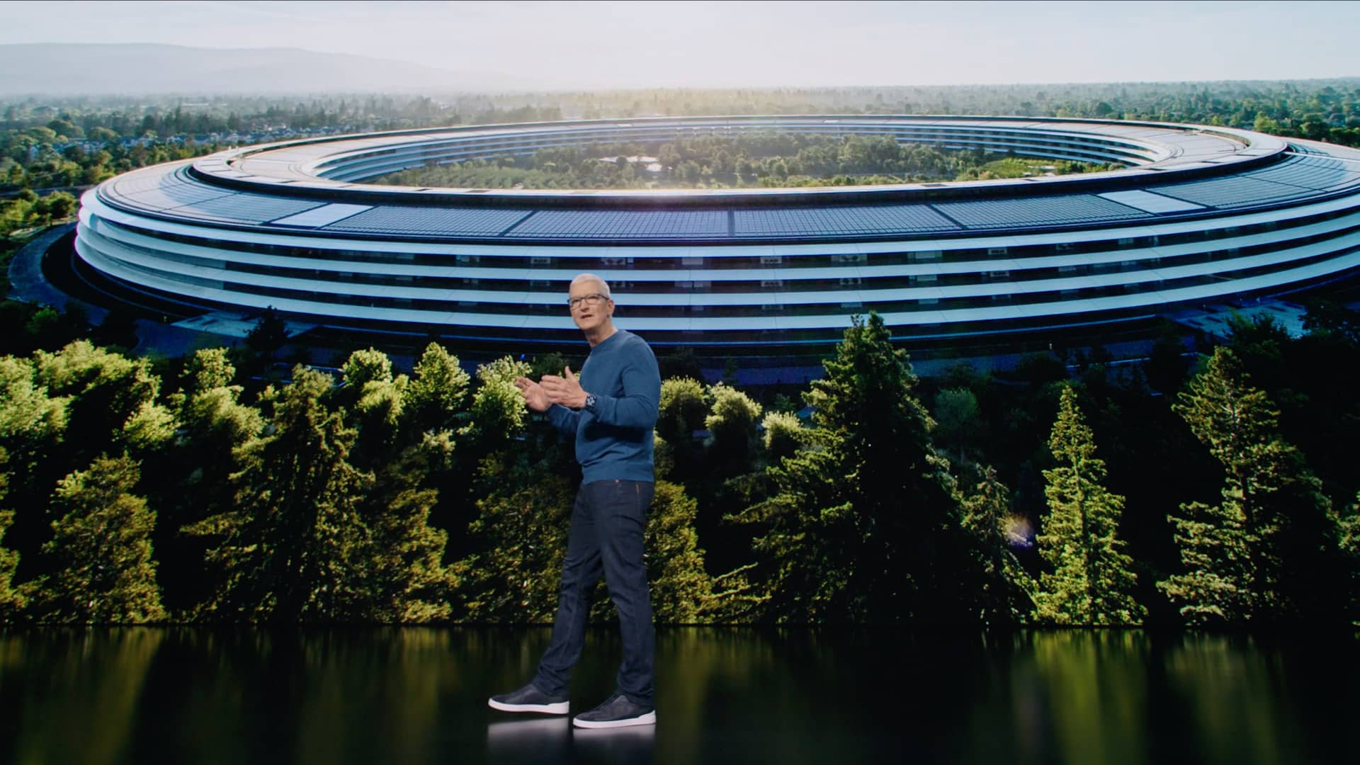 A still image from Apple's September 2021 “California Streaming” event video with CEO Tim Cook standing on stage in front of a huge keynote slide behind him that displays an aerial view of the Apple Park headquarters while Cook is talking enthusiastically and gesturing with his hands