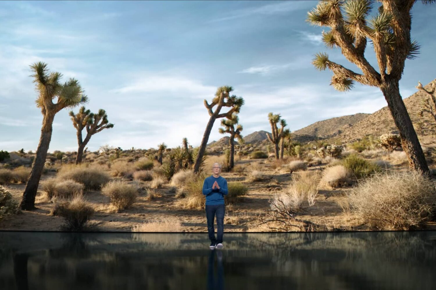 A still image taken from Apple's September 2021 “California Streaming” event video which shows CEO Tim Cook walking toward the audience with his hands in praying position. In the background behind him, a huge slide displays an image of a California desert.