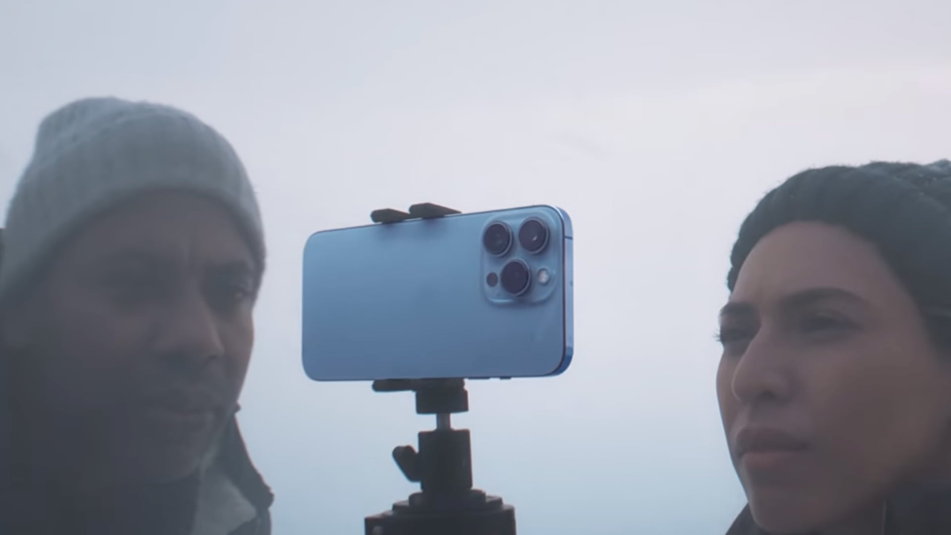 A still image taken from Apple's iPhone 13 Pro introduction video on YouTube, showing a closeup of two crew members shooting a winter scene using a tripod for the handset
