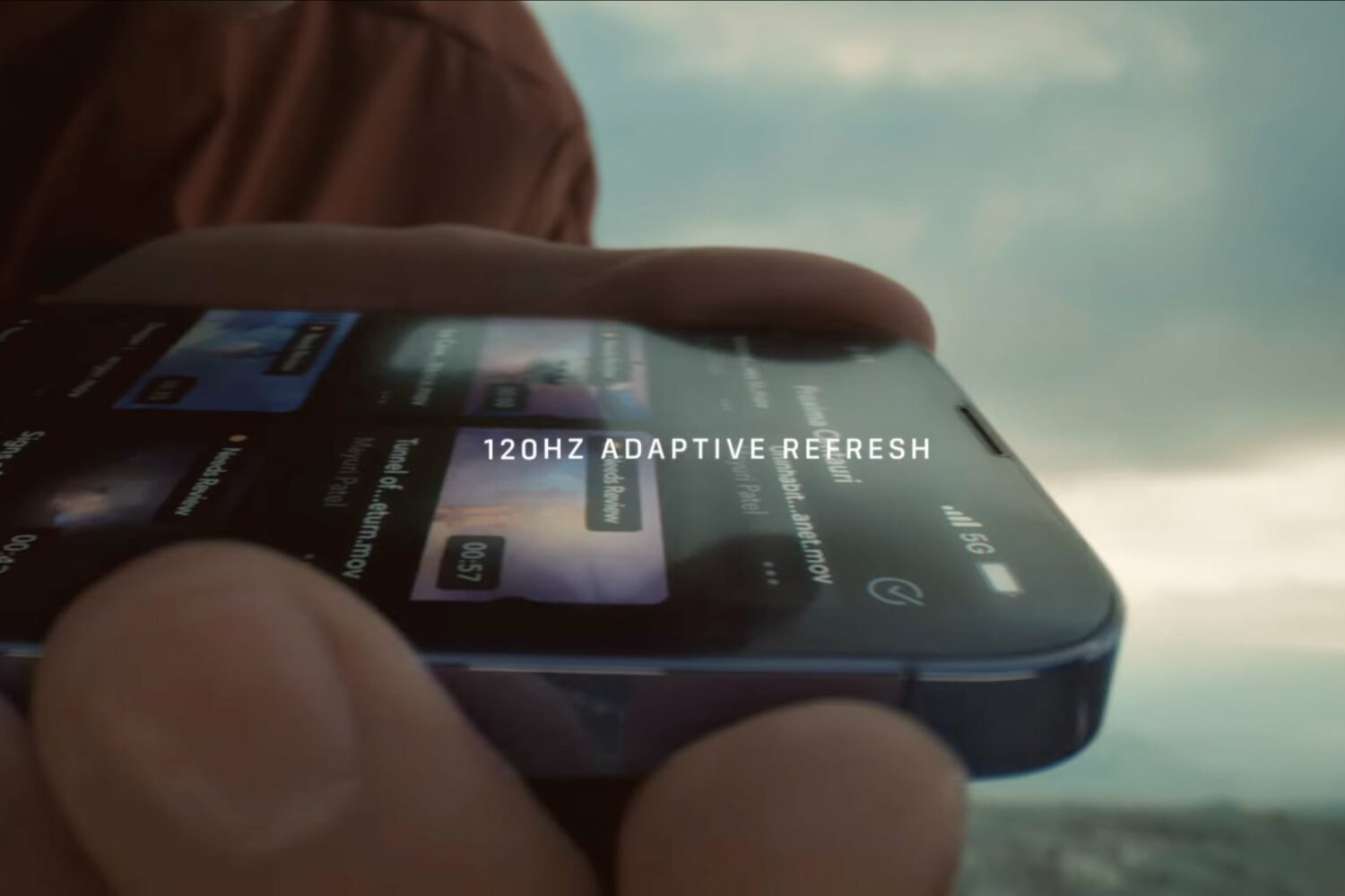 Image from Apple's YouTube video showing ProMotion technology in action, with a hand holding an iPhone 13 Pro and scrolling through a list and the title "120Hz adaptive refresh rate" overlaid on top