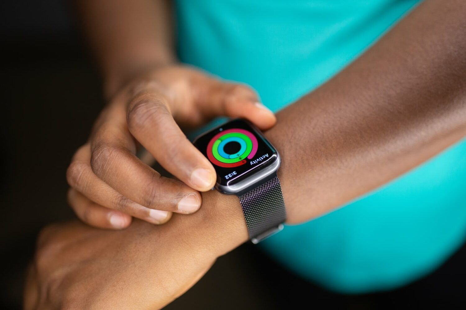 A closeup photograph of a female athlete's hand wearing an Apple Watch showing the Move, Exercise and Stand rings nearly closed