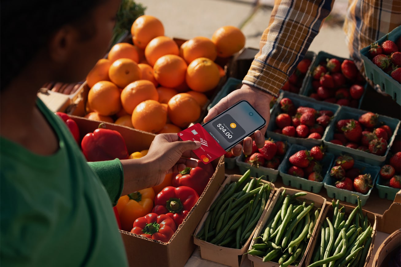 Apple's marketing image showing a young woman touching her iPhone with an NFC-enabled credit card to use the Tap to Pay contactless payments feature in Apple Pay