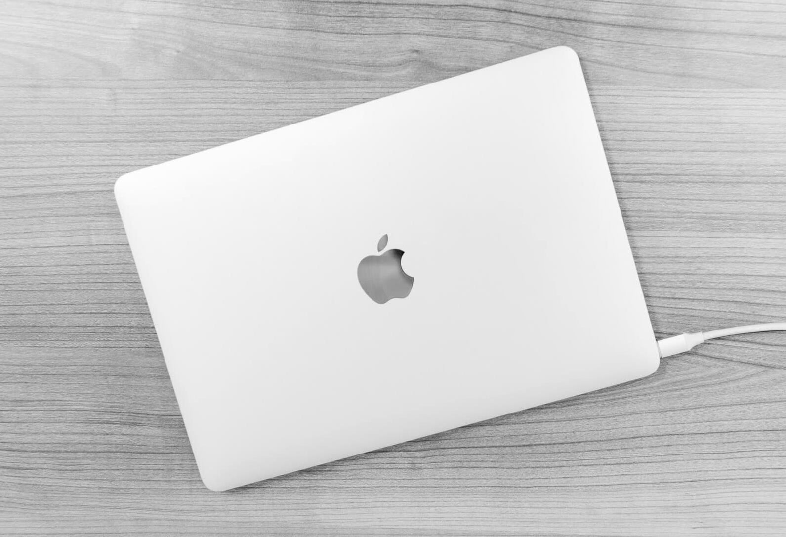 Black and white picture of a MacBook kept on table and charging