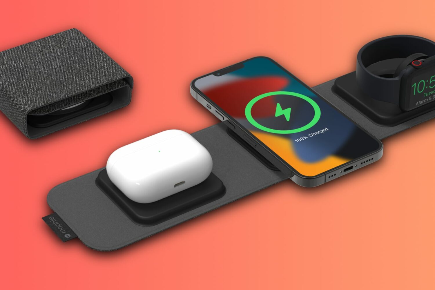 A rendering showing an isometric view of Mophie's 3-in-1 travel charger with AirPods, iPhone and Apple Watch resting on its charging pads, set against a light orange gradient background
