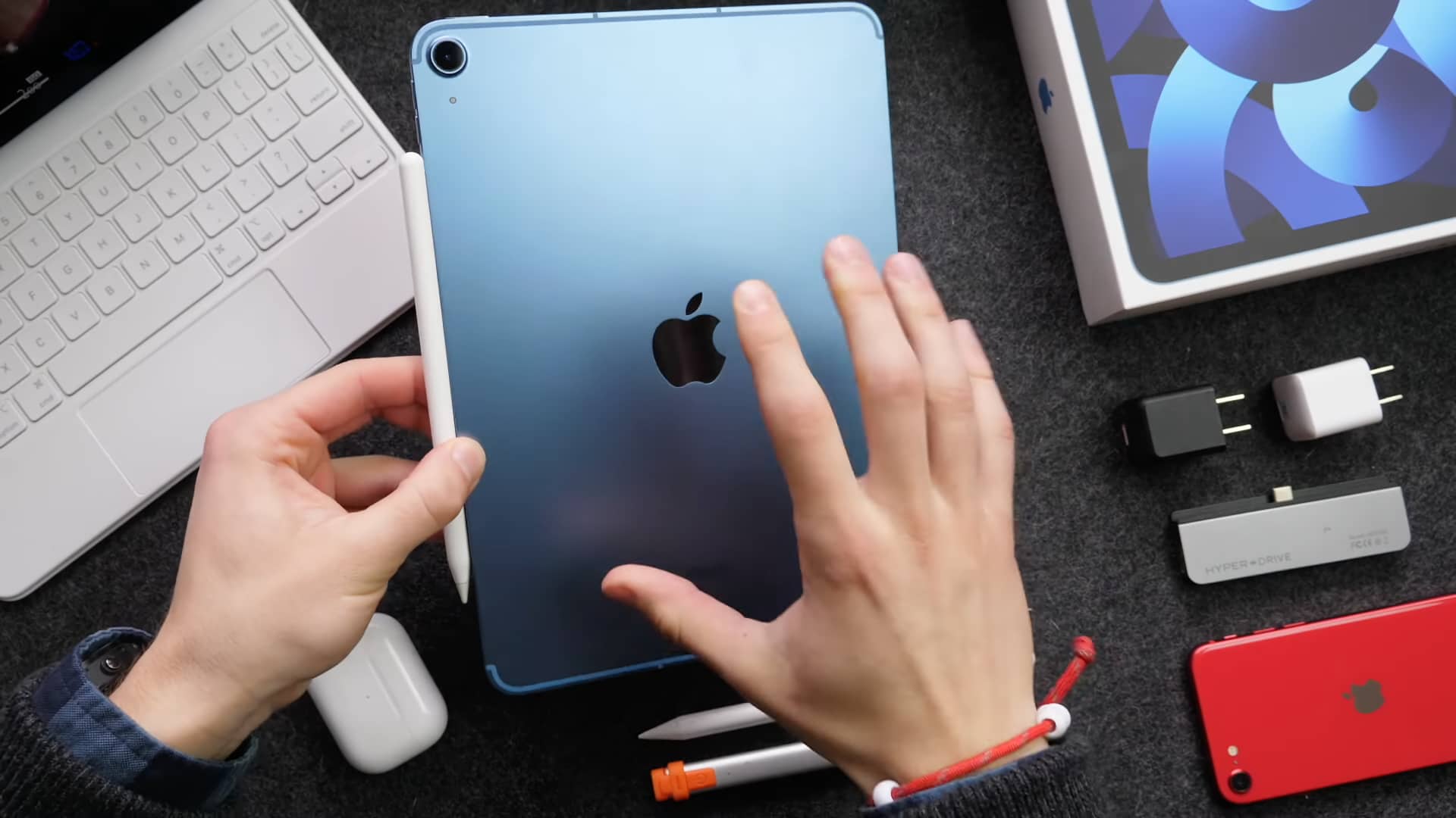A top-down photograph showing a young male's left hand holding a blue iPad Air 5 with their right hand's fingers spread across the back of the tablet