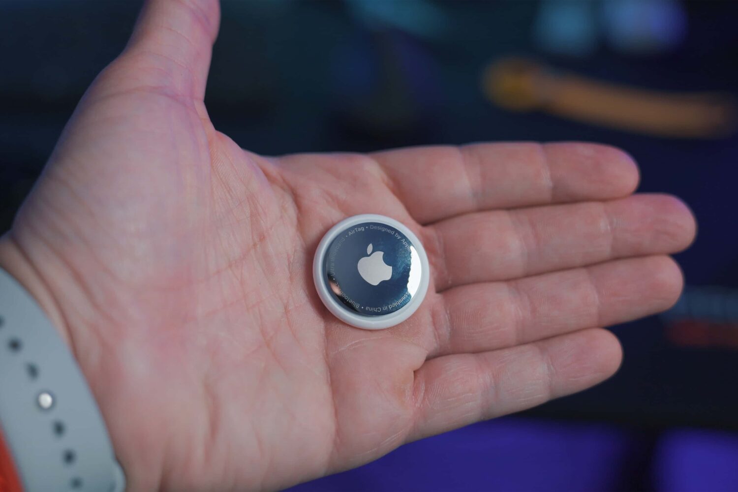 A photograph of an Apple AirTag in the palm of a male's hand