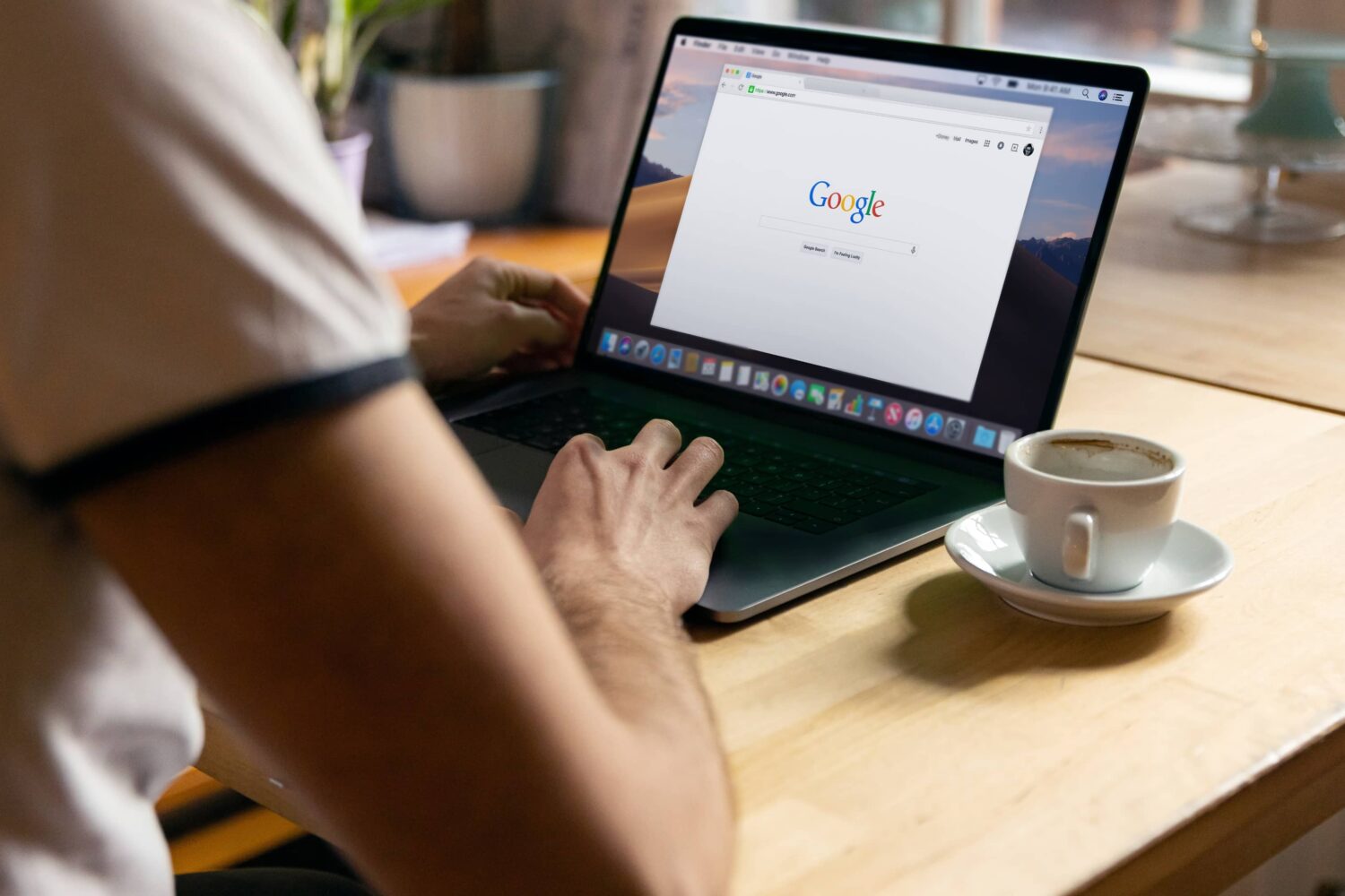 A lifestyle photograph showing a young male from behind, sitting in front of a MacBook Pro with the Chrome browser running on the Google search page