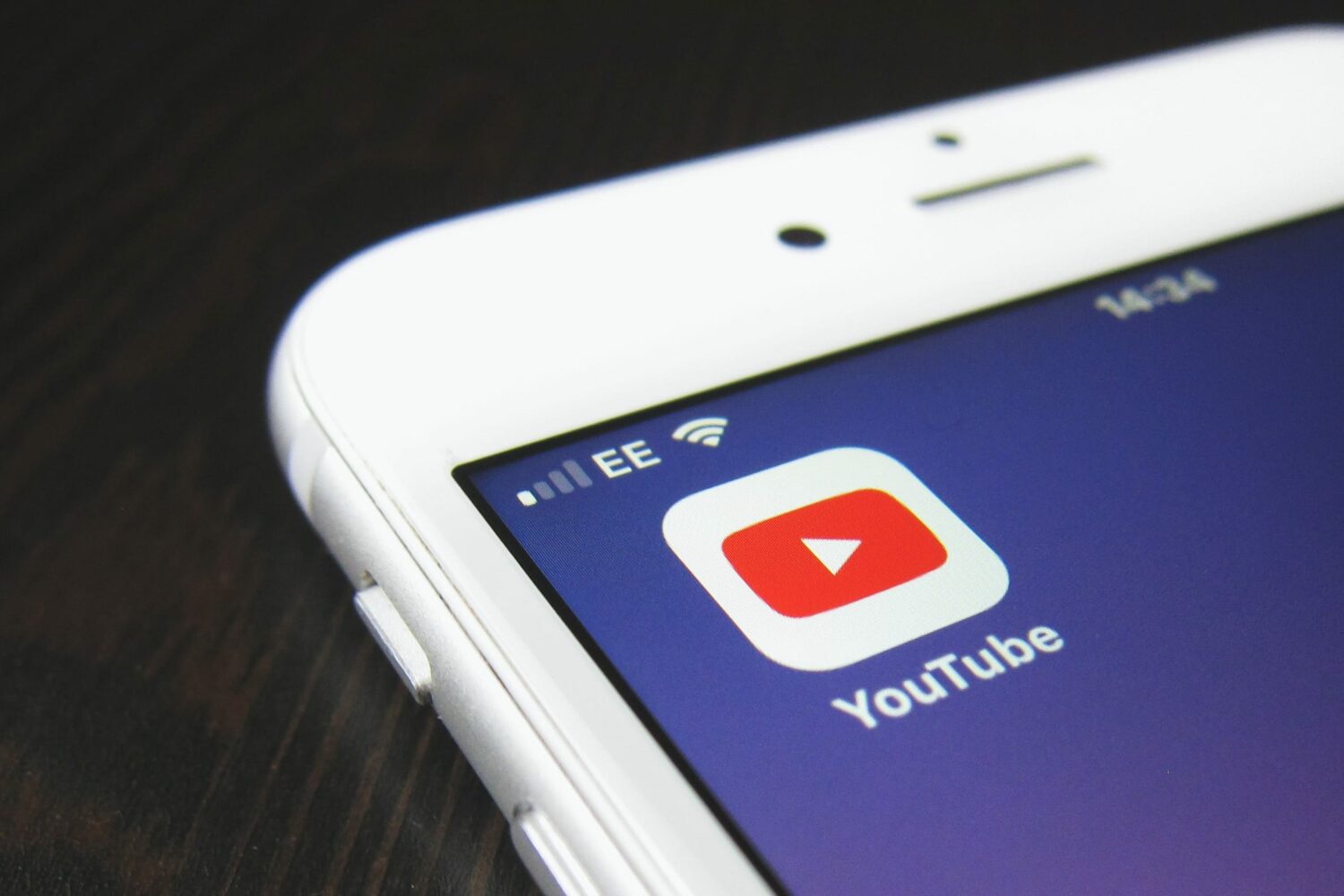 A closeup photograph of a white iPhone with an icon for the Google YouTube app displayed on the home screen