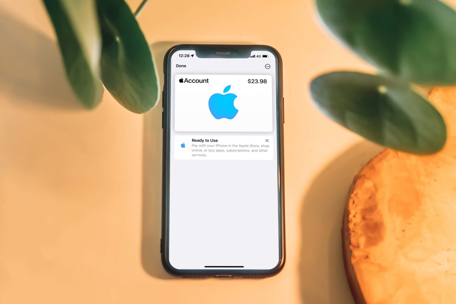 This mockup depicts an iPhone which is laid flat on a table, running the Wallet app. A banner in Wallet confirms that an Apple Account card has been successfully added to Apple Pay. The message informs the user they can use this virtual card when buying physical products at Apple stores, as well as apps, media and subscriptions online.