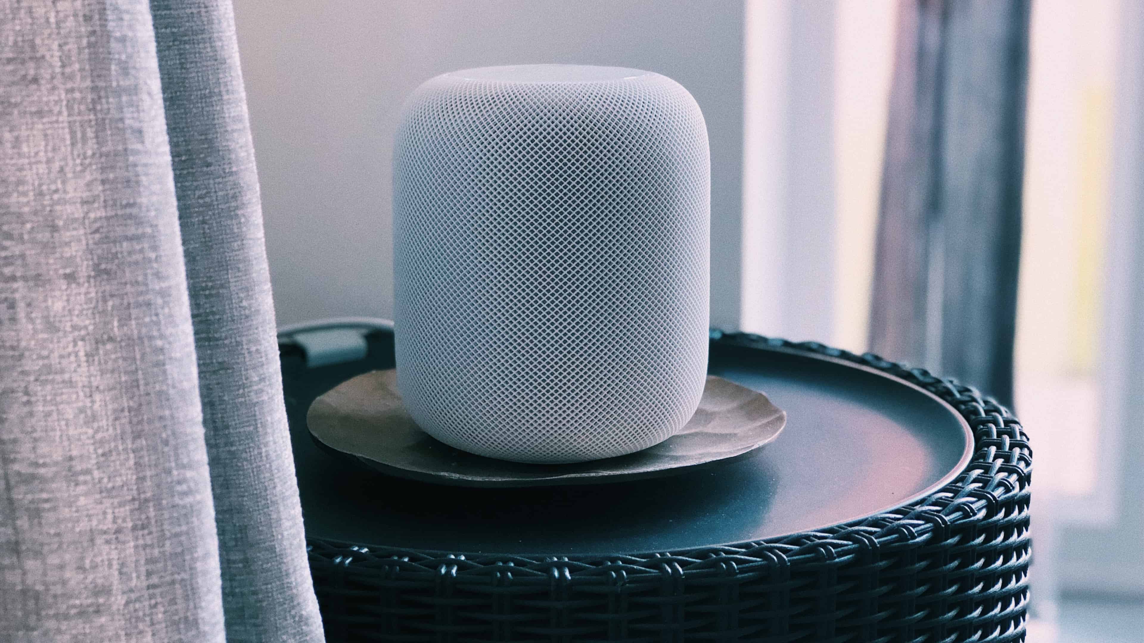 A silver version of Apple's full-size HomePod wireless speaker is shown sitting on a table in this photo from Unsplash