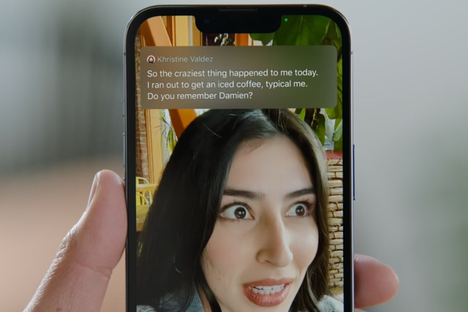 A photograph showing an iPhone held in a person's hand, demonstrating the Live Captions feature in action during a FaceTime video call