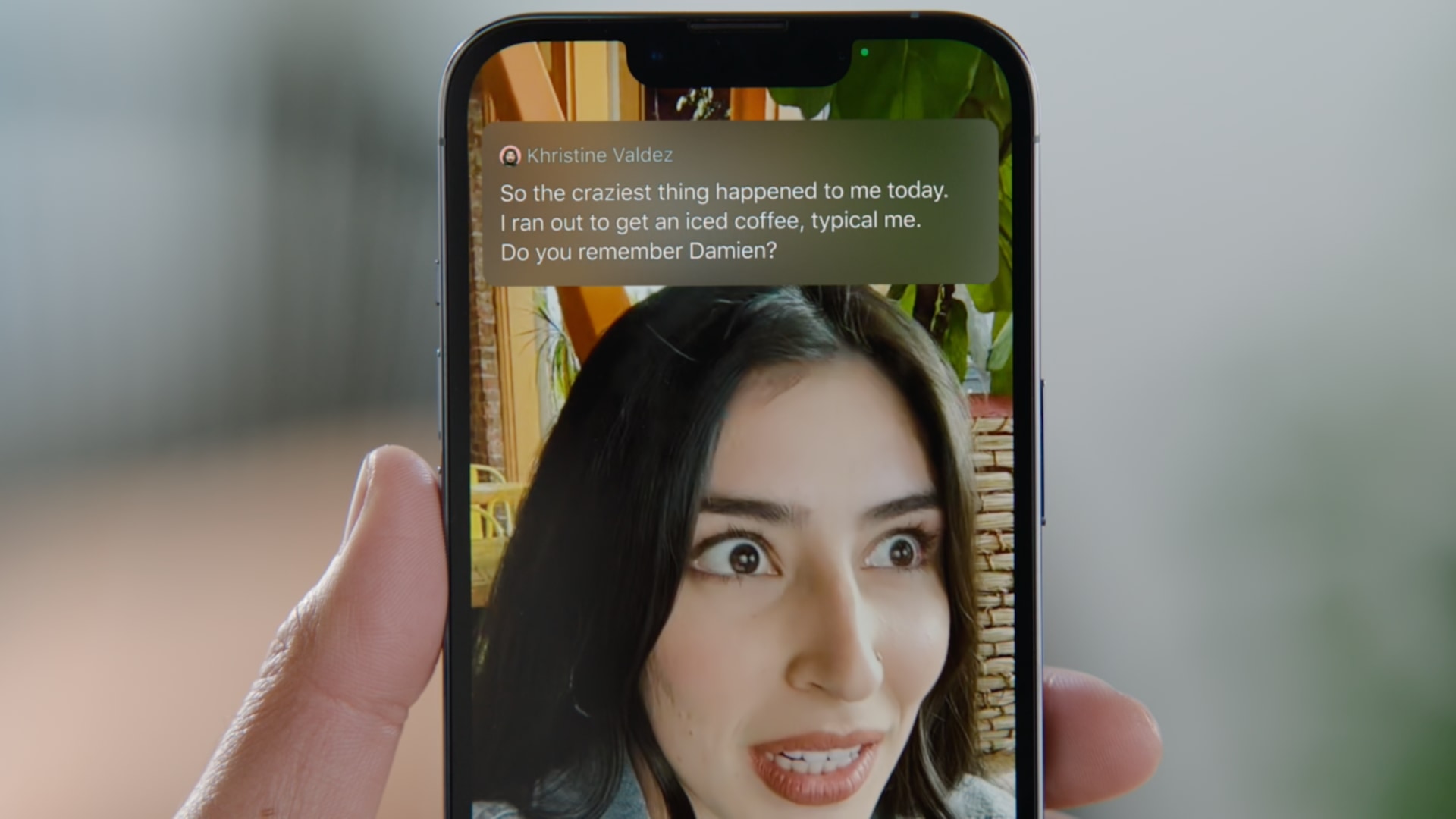 A photograph showing an iPhone held in a person's hand, demonstrating the Live Captions feature in action during a FaceTime video call 