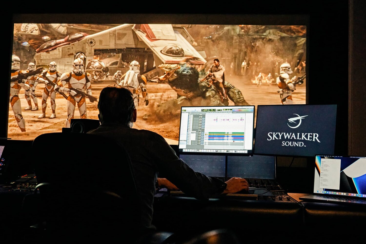 A photograph showcasing an engineer sitting behind a mixing pull on Lucasfilm's Skywalker Ranch and using Macs to create sound effects for a Star Wars scene