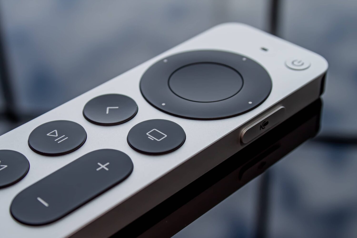 A redesigned Siri-powered remote for the Apple TV streaming box is shown laid flat on its back on a glass table in this close-up photograph.