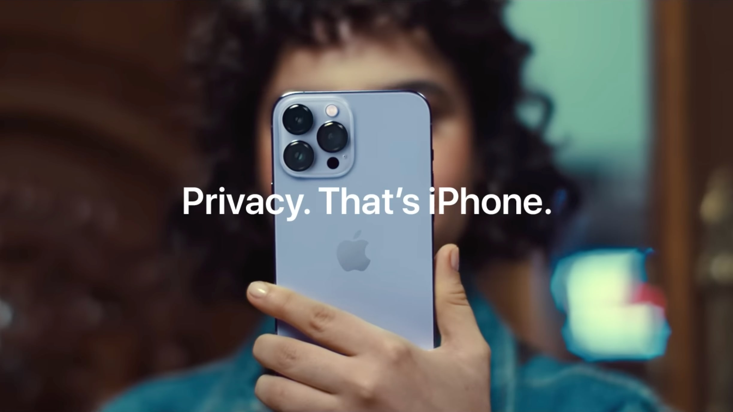A scene from Apple's video commercial showing a woman's face obscured by an iPhone 13 Pro Max she's holding in front of her face, with the tagline "Privacy. That's iPhone" overlaid on top