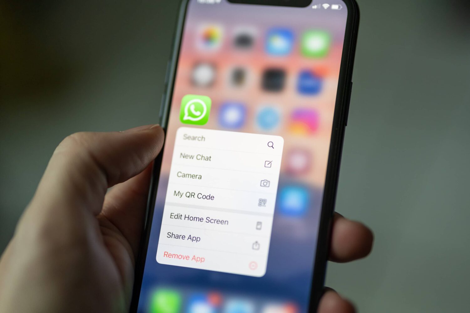 Apple's iPhone displaying the home screen shortcuts menu for WhatsApp is being held in a male's hand in this featured image from Unsplash