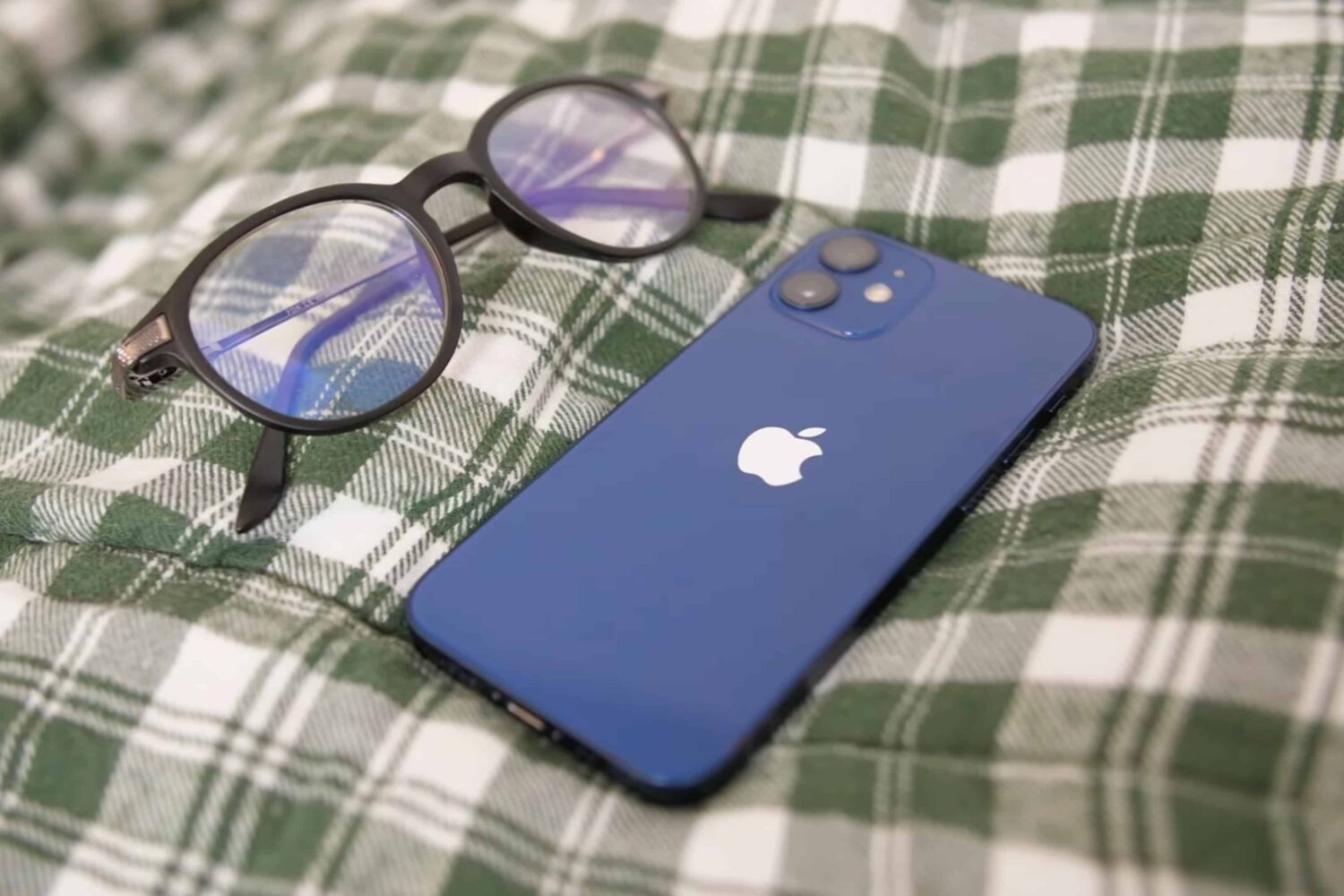 Apple's iPhone 13 laid next to glasses is being featured in this closeup photo, illustrating the ability to silence all iPhone notifications when the device is face down or covered