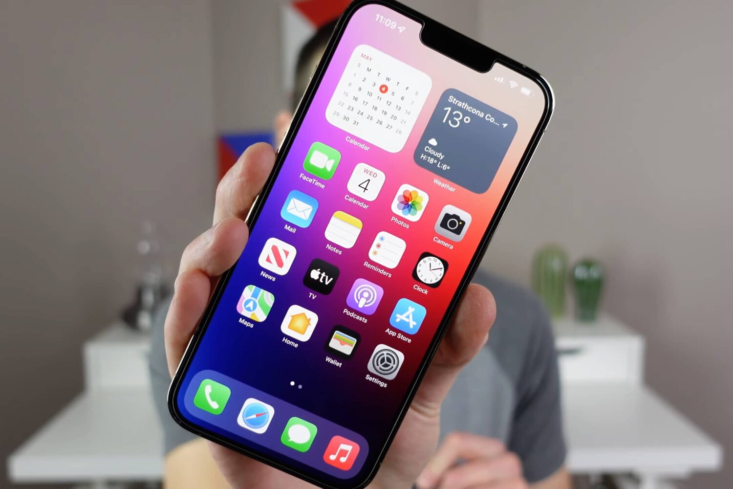 Apple's iPhone 13 Pro Max with home screen widgets and app icons is being held in front of the camera in this still image screenshotted from iDownloadBlog's video walkthrough covering 15 iPhone settings designed for optimal experience