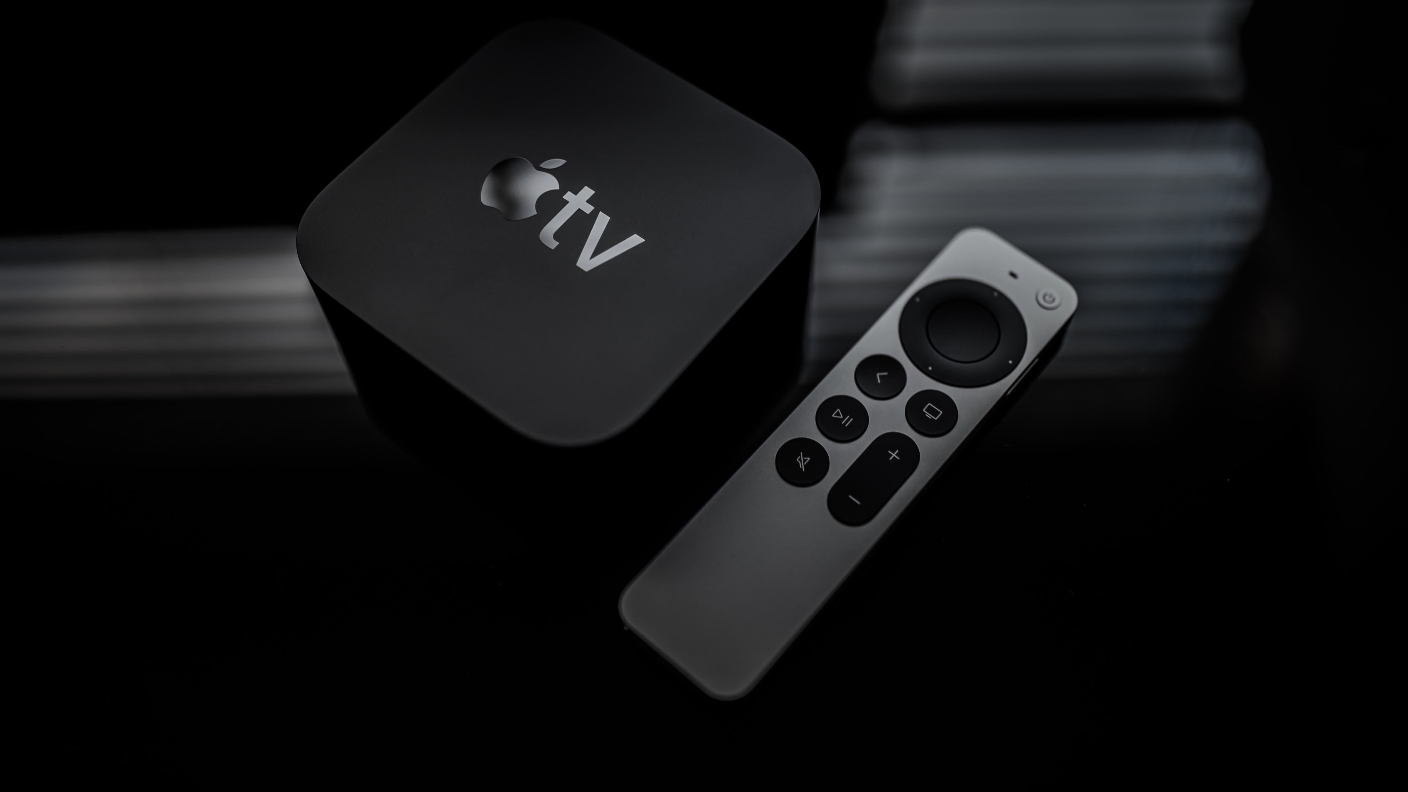 An angled top-down view of a second-generation Apple TV 4K along with an updated Siri Remote, set against a dark background