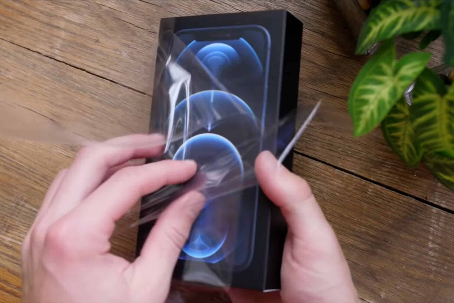 A still image from an iPhone 12 unboxing video that shows unwrapping the plastic wrapping of Apple's packaging for the phone