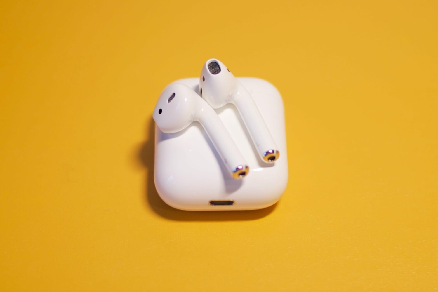 Apple AirPods resting on their charging case, set against a yellow solid background