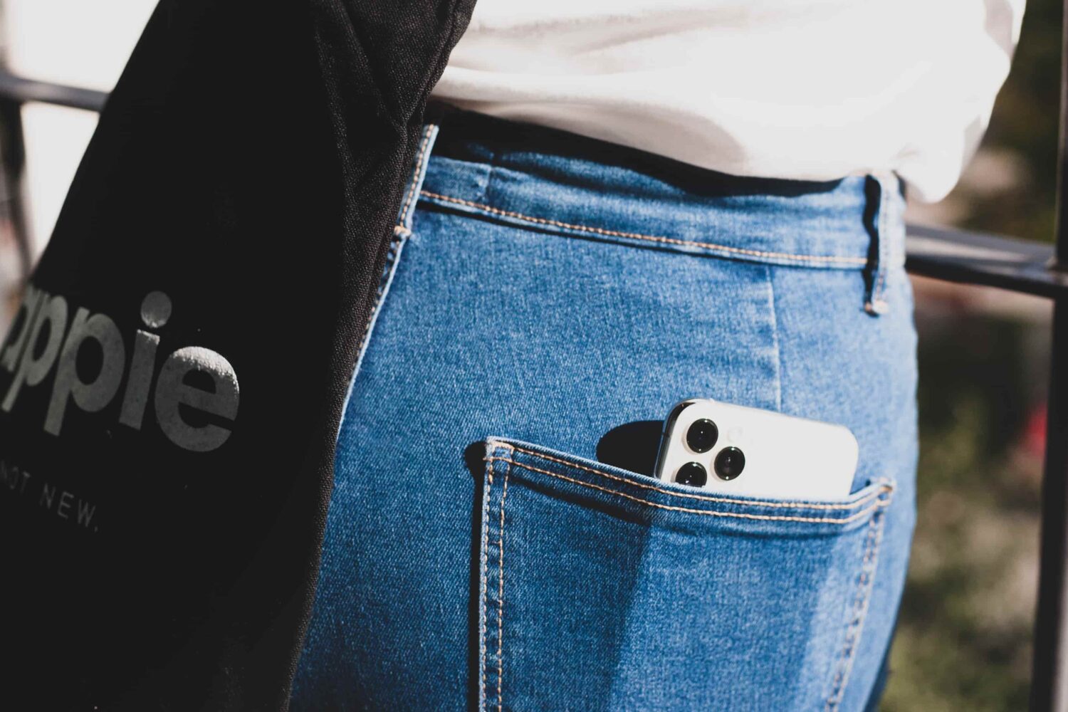 Closeup of a woman's back jeans pocket with a white Apple iPhone 13 Pro inside