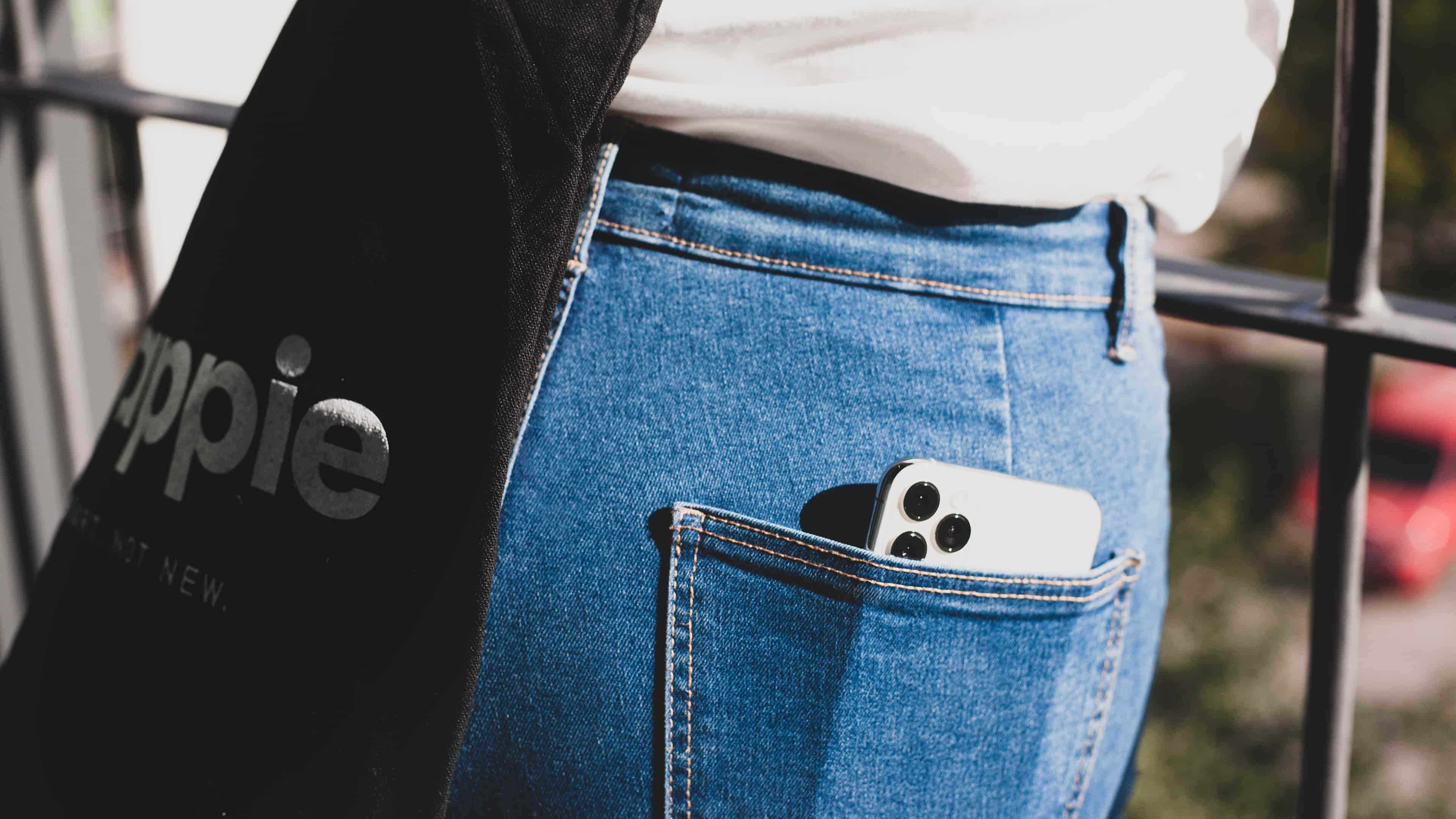 Closeup of a woman's back jeans pocket with a white Apple iPhone 13 Pro inside
