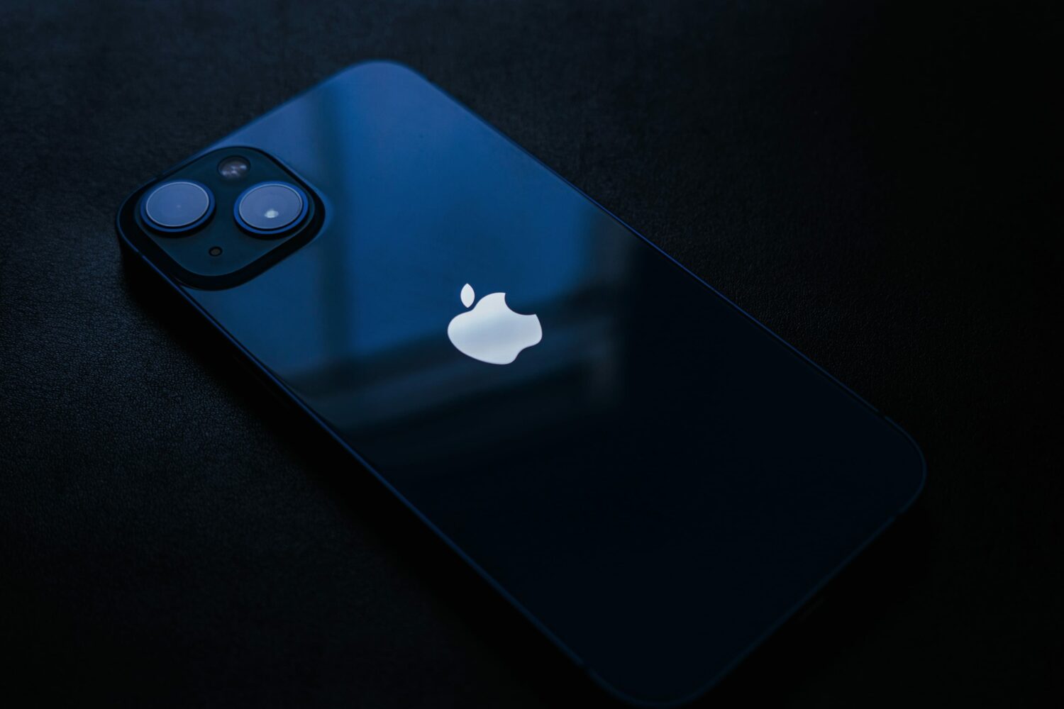 Blue iPhone 13 set facedown on a laptop sleeve on the bed