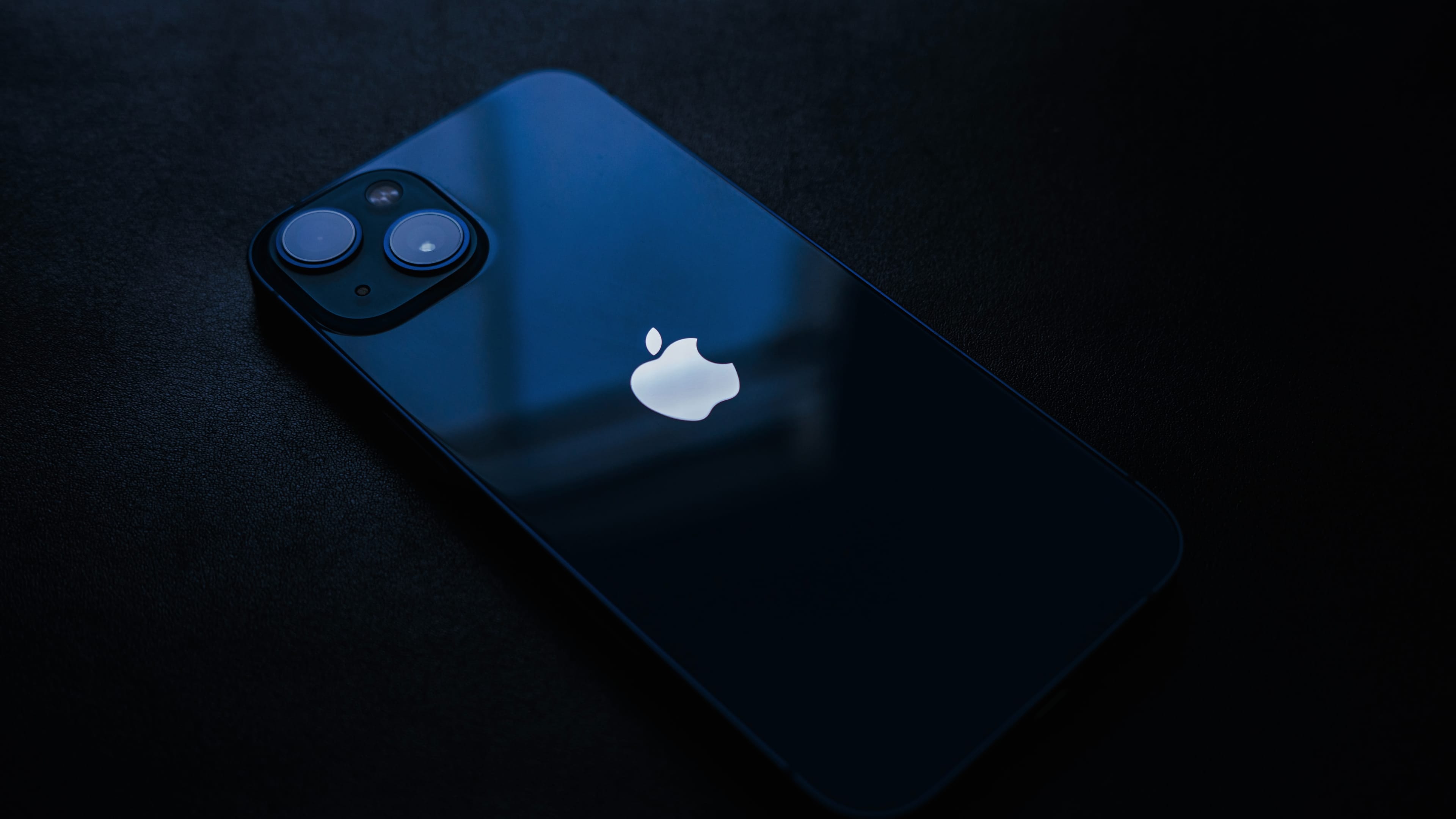 Blue iPhone 13 set facedown on a laptop sleeve on the bed