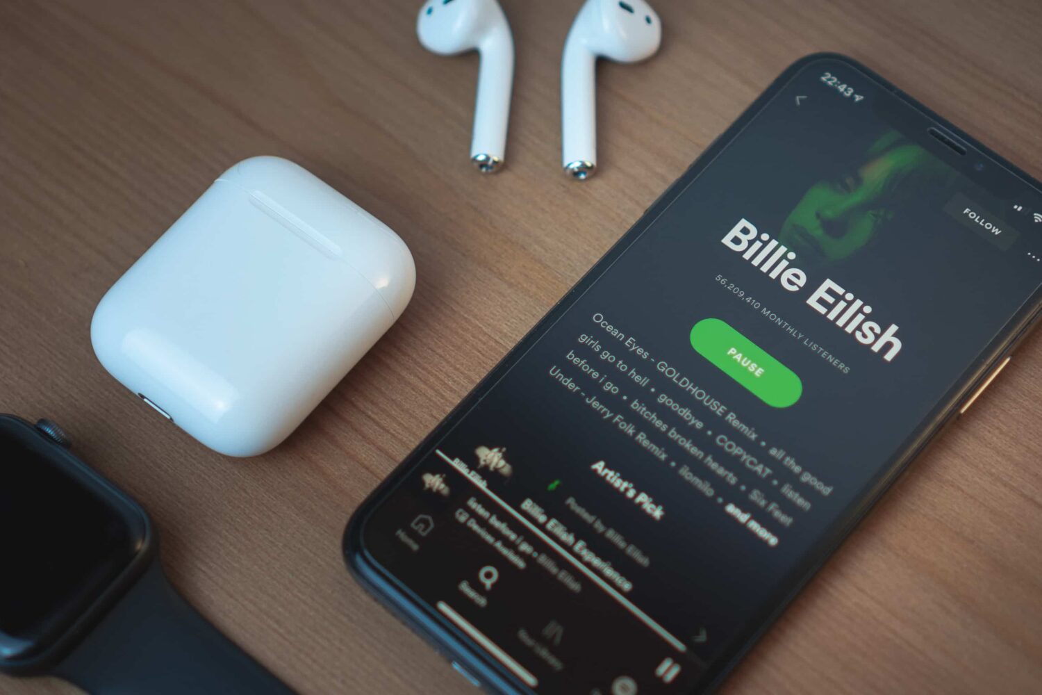 An iPhone running Spotify laid flat on a table alongside AirPods and an Apple Watch