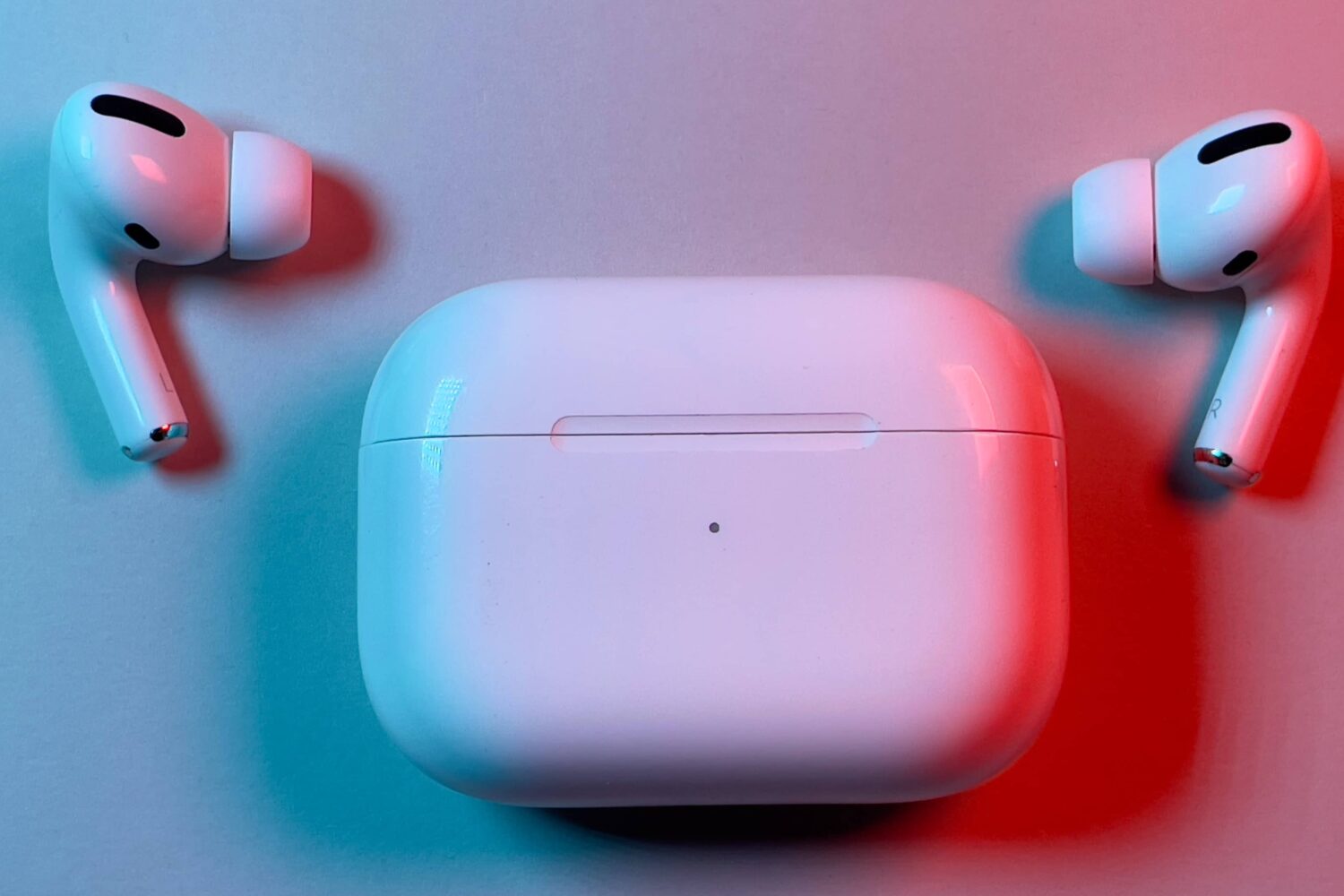 AirPods Pro earbuds lying next to a charging case with the lid closed