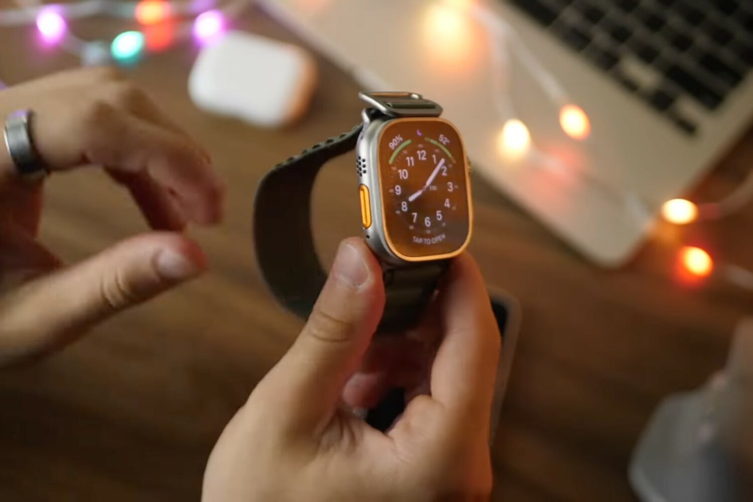 A young male's hand holding Apple Watch Ultra with the Alpine Green Loop band, with the orange Yellow button visible