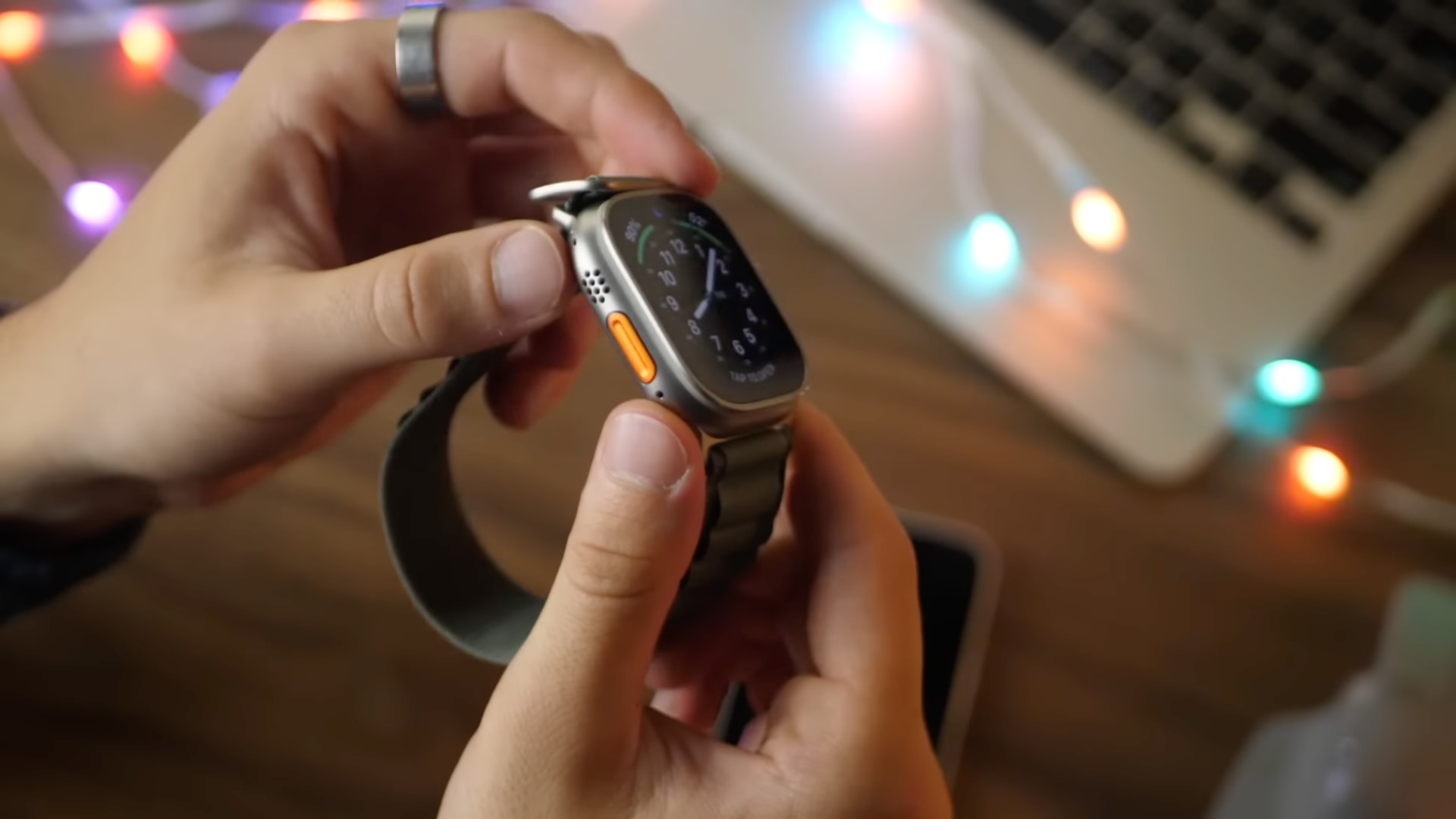 Young male hands holding Apple Watch Ultra in the Alpine Green Loop band, with the orange Yellow button visible
