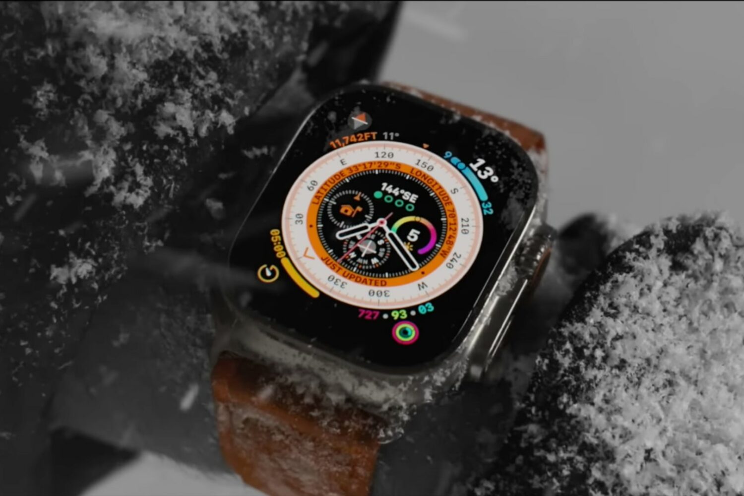 Apple Watch Ultra on a mountain climber's wrist under heavy snow, displaying stats on the Wayfinder face