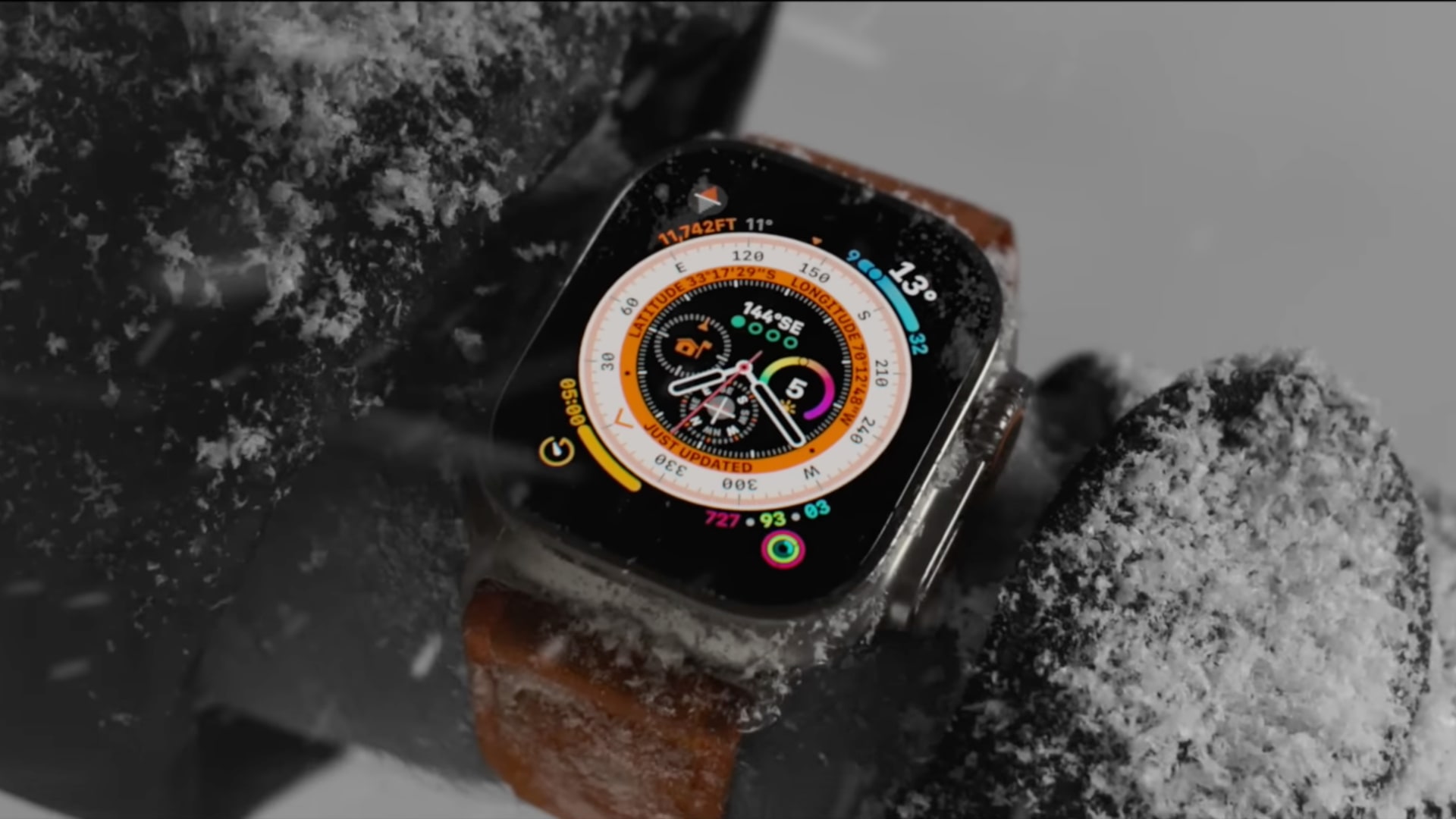 Apple Watch Ultra on a mountain climber's wrist under heavy snow, displaying stats on the Wayfinder face