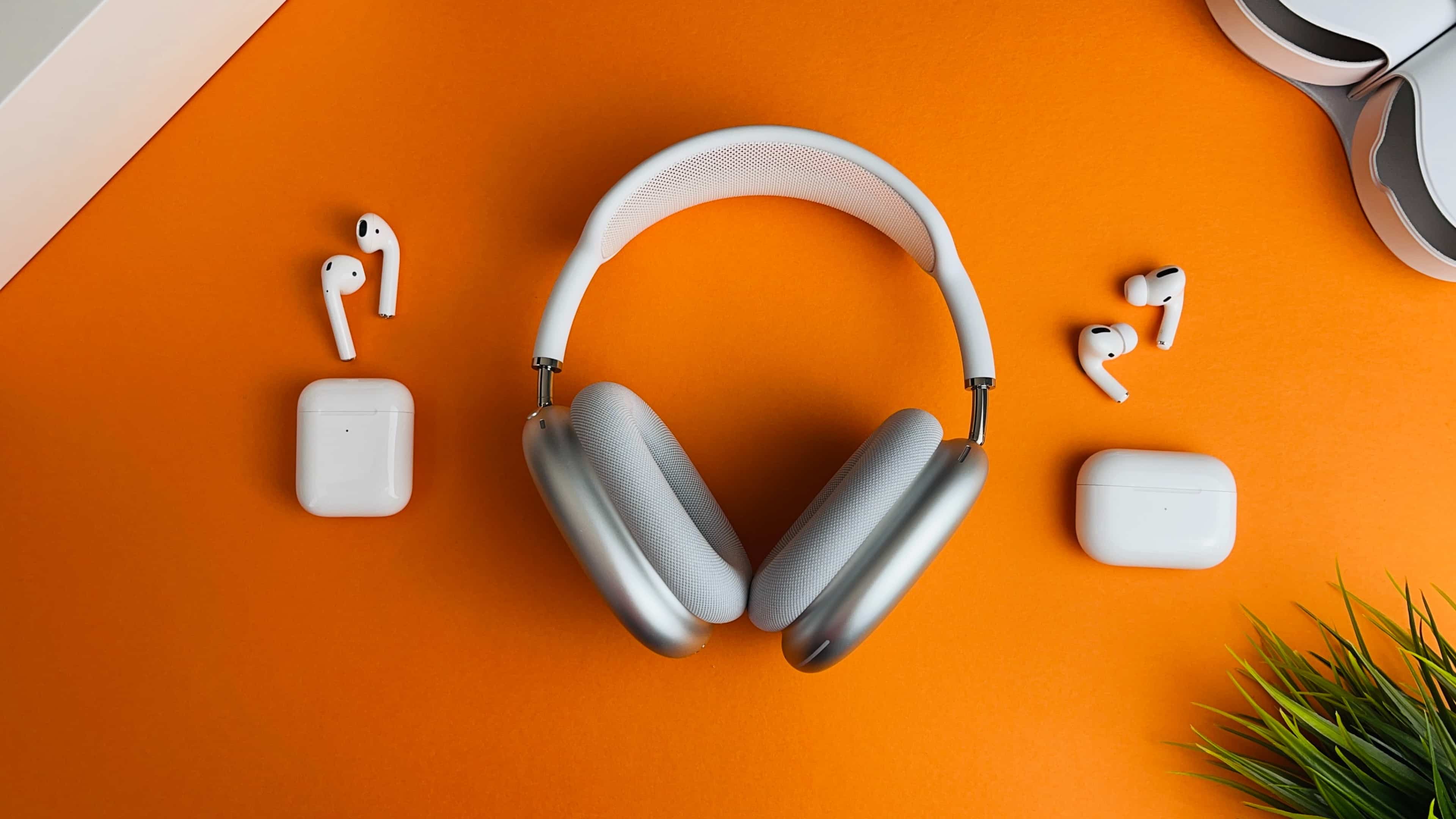 AirPods Max, the original AirPods and the first AirPods Pro laid flat on an orange table