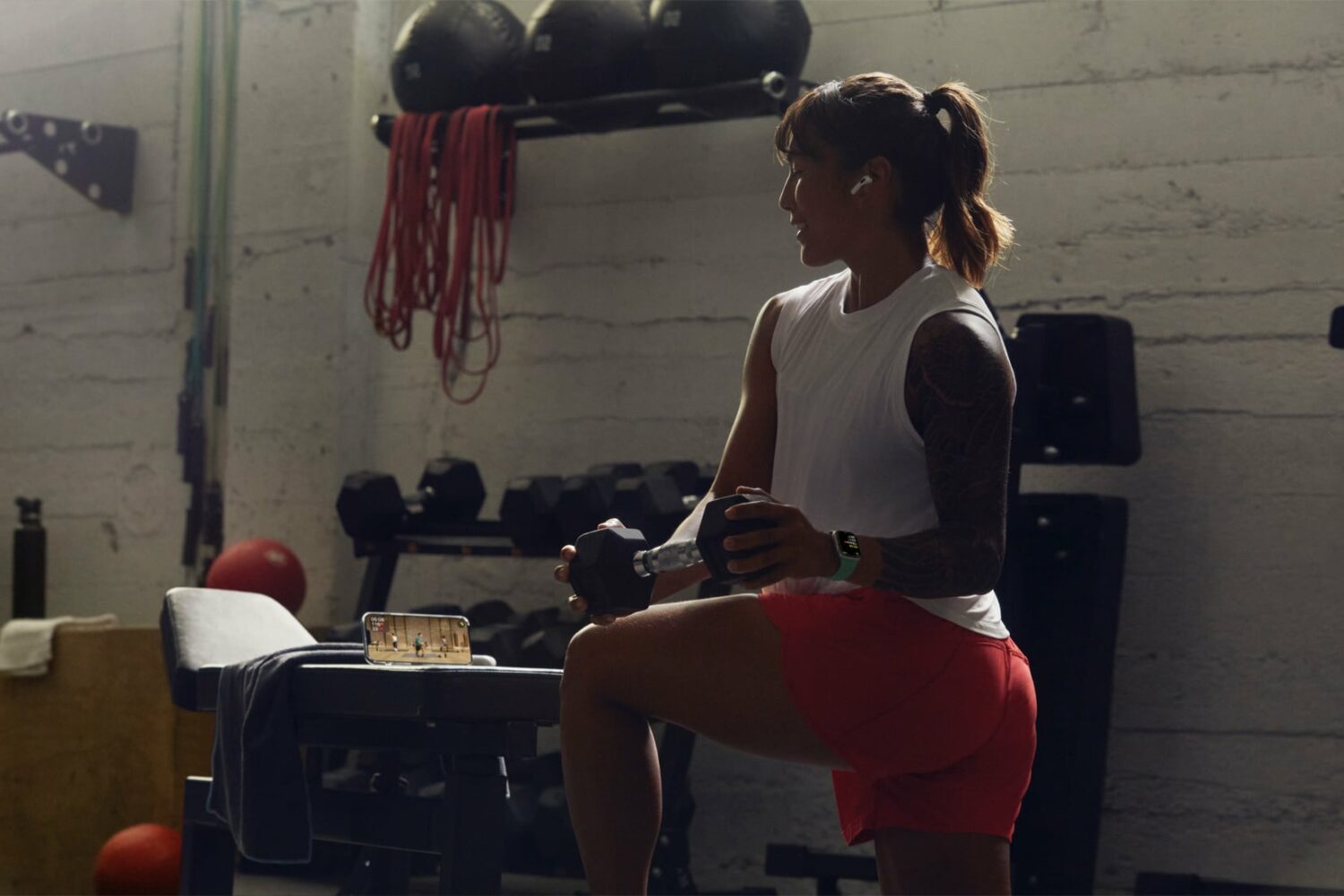 A young woman in a gym following her strength workout via Fitness+ on iPhone