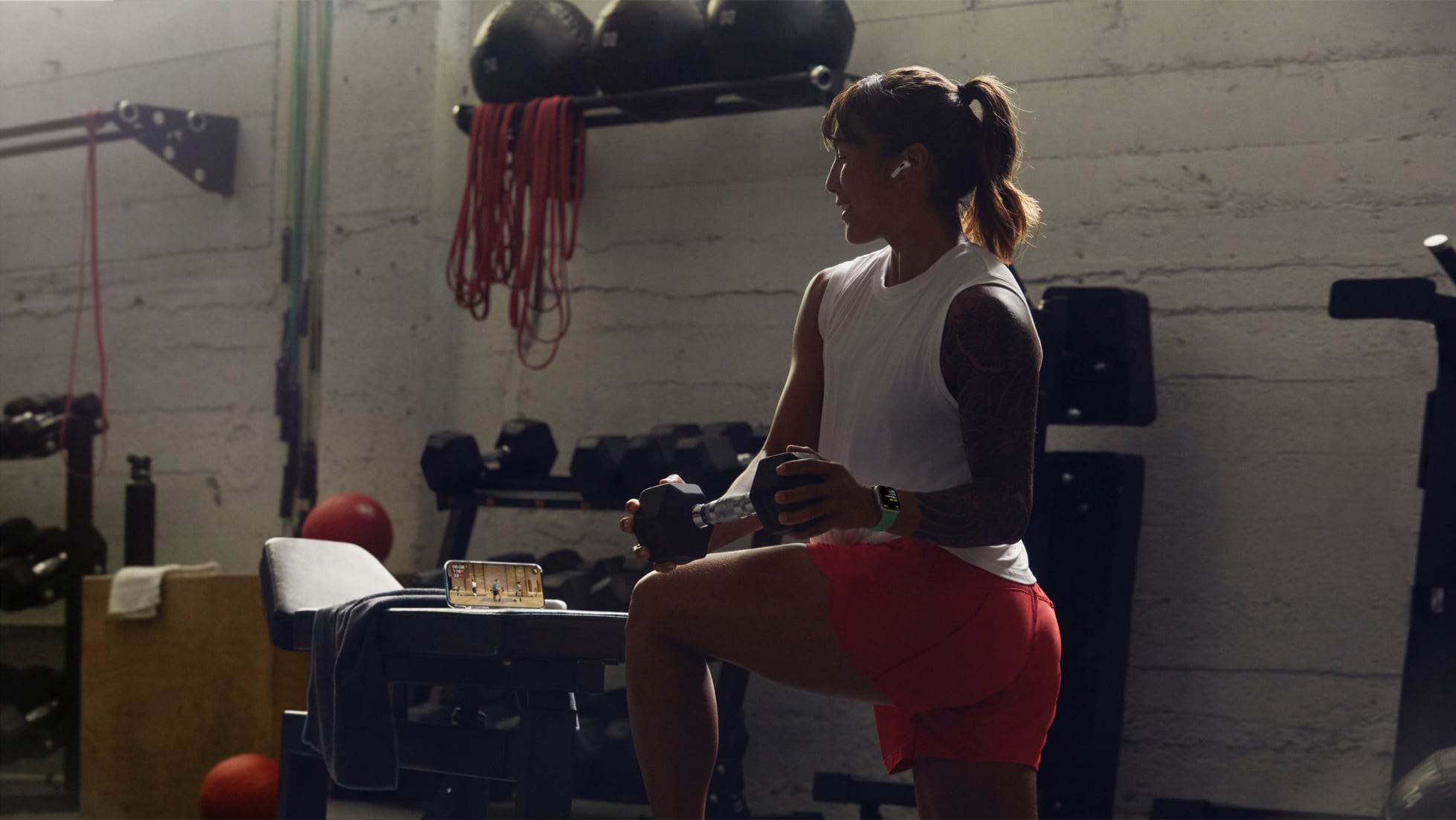 A young woman in a gym following her strength workout via Fitness+ on iPhone